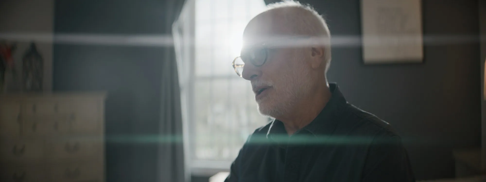 An older man sitting in bright daylight at home