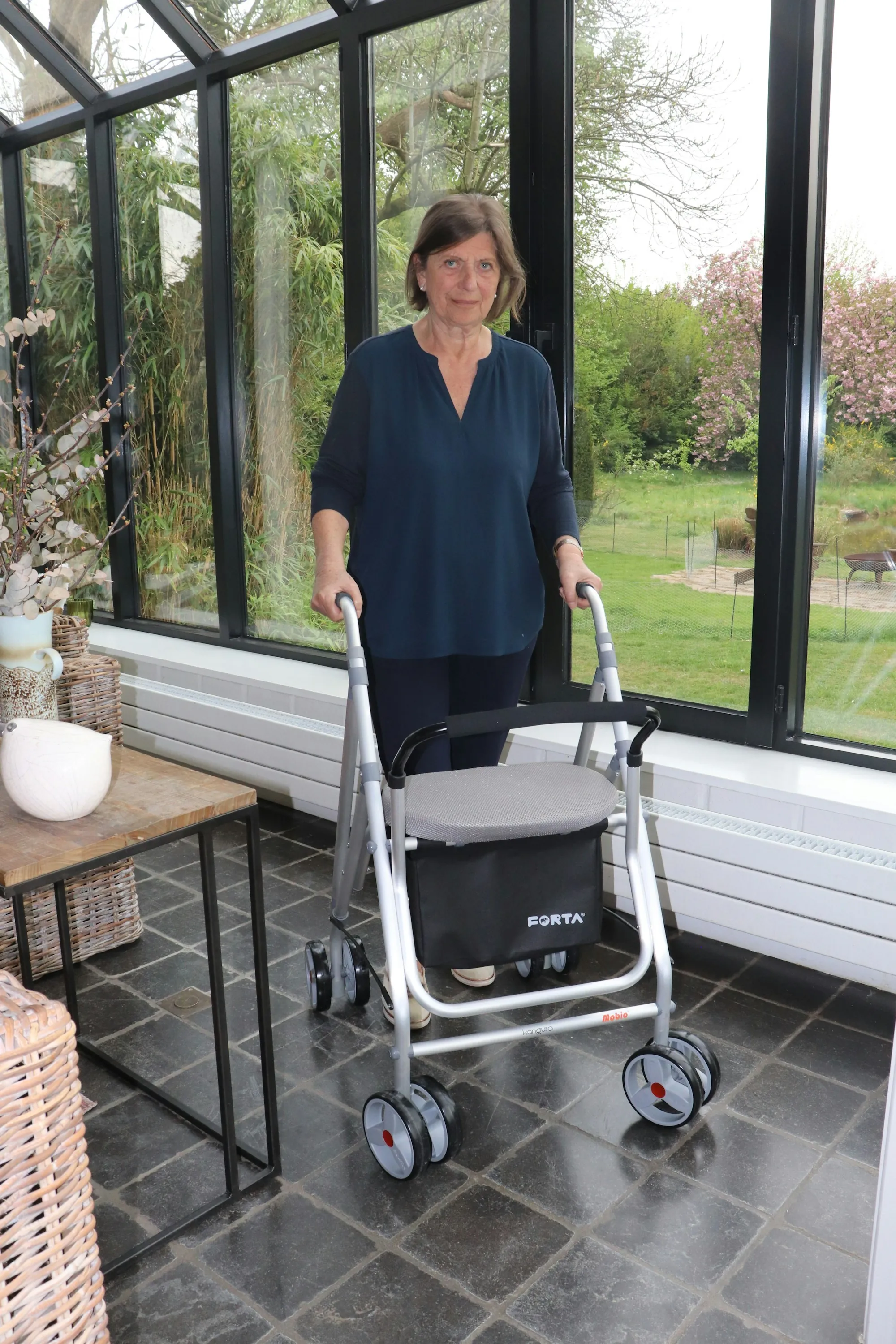 A woman using a walking frame in a bright sunroom